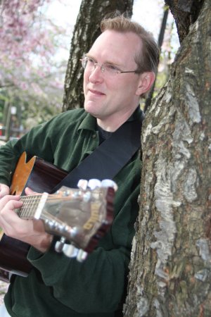 Mark Shepard, Transformational Songwriter playing guitar next to a tree